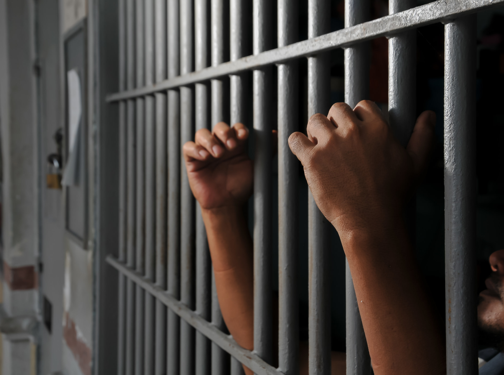Mãos de detento nas grades de uma cela